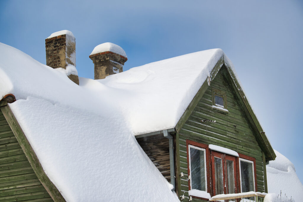 Roof is heavily covered in white snow, with two chimneys